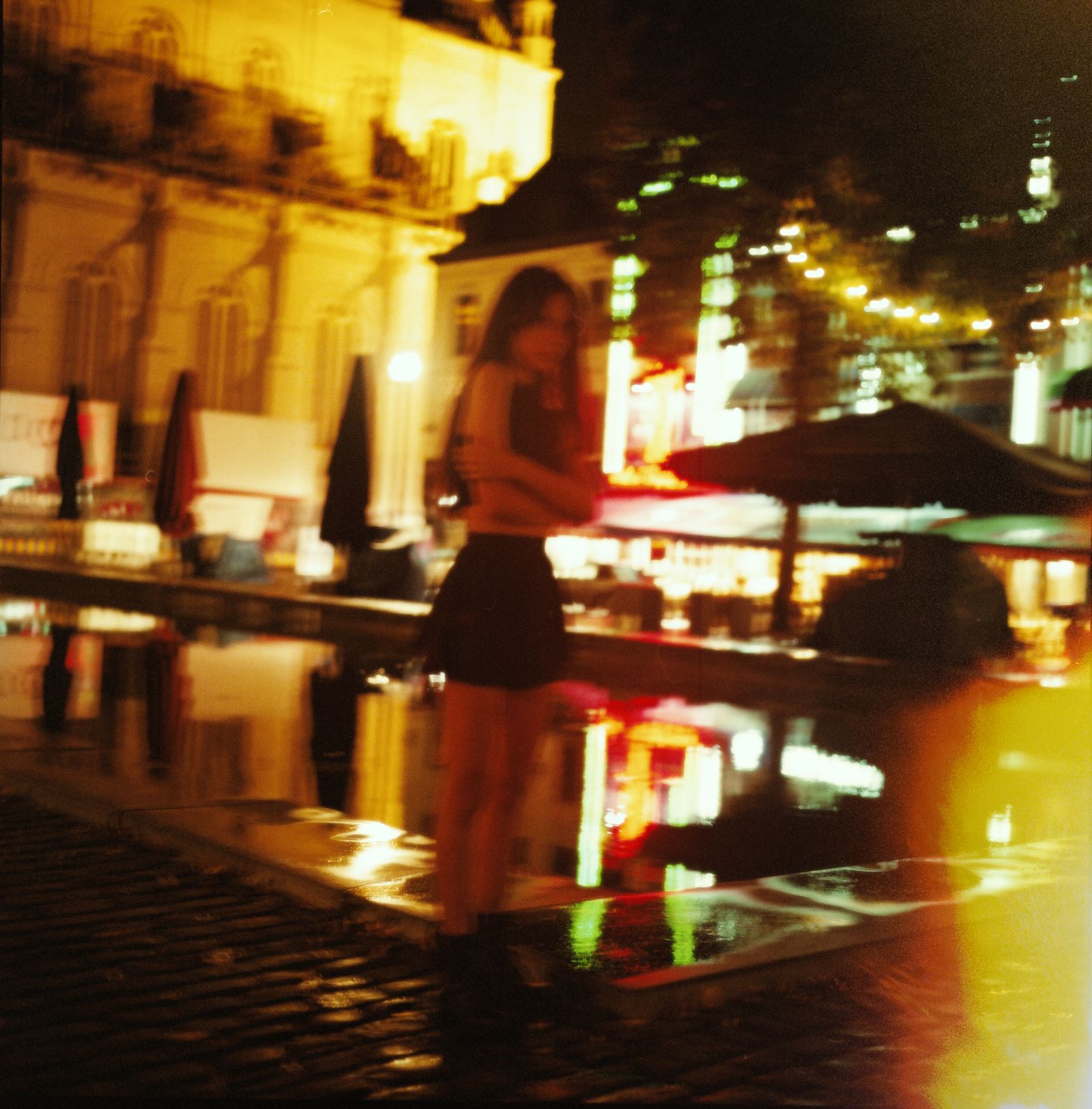 A woman in a black top standing against a dark, illuminated office building at night