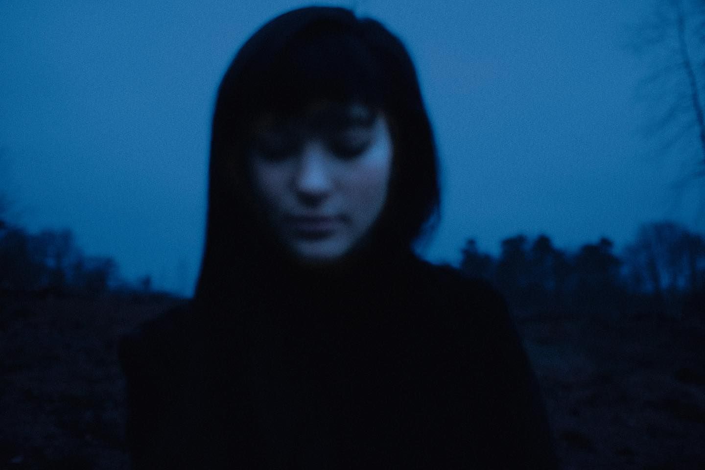 A red-lit face glowing against bare branches and a dusk sky