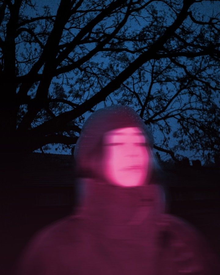 A face lit hot pink under a glowing tent at a fairground at night