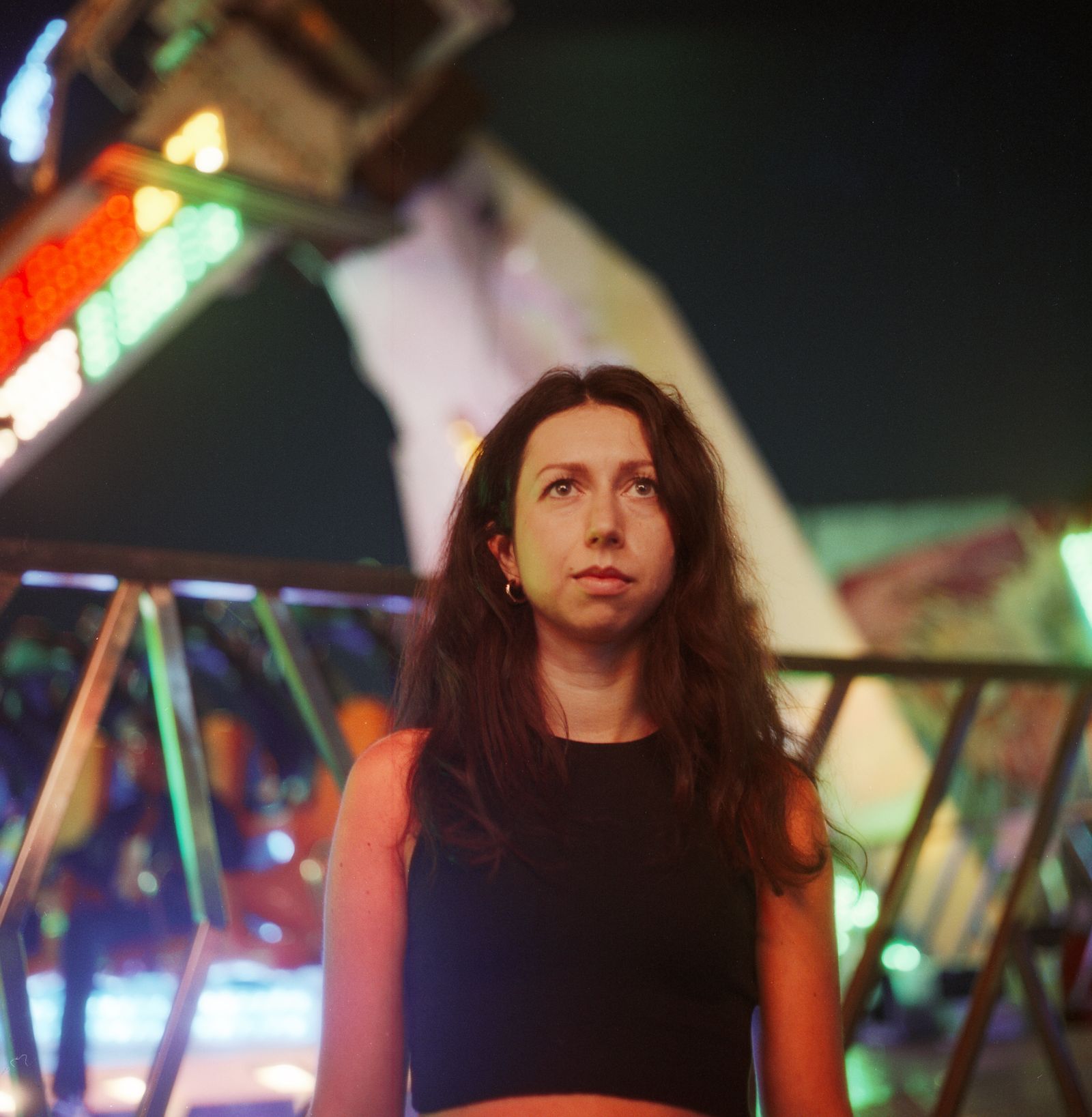 A close portrait beneath a fairground ride, ferris wheel lights blurred in the background
