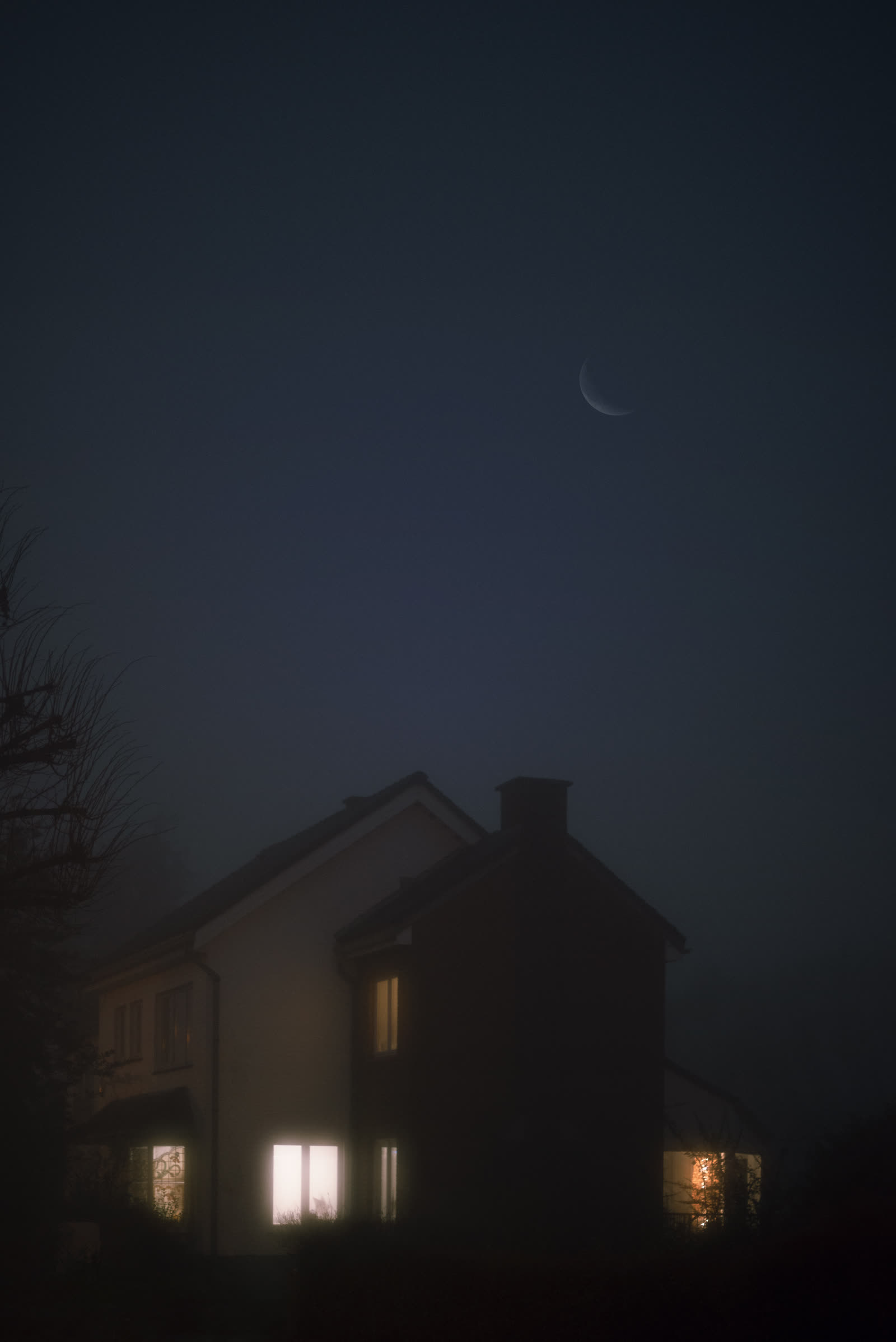 A house silhouette at dusk, scattered lit windows under a crescent moon