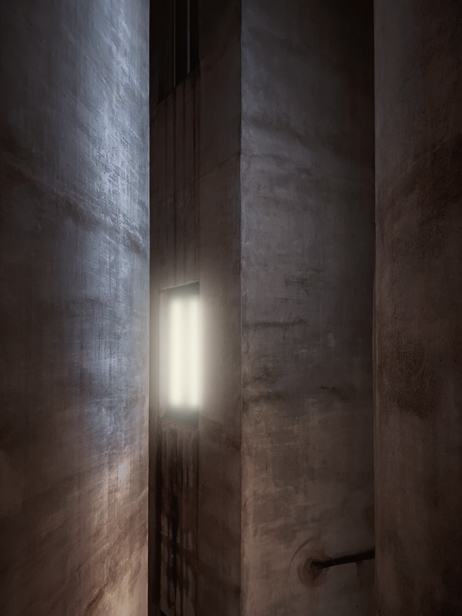 A narrow gap between concrete walls, one window glowing white at the end of it