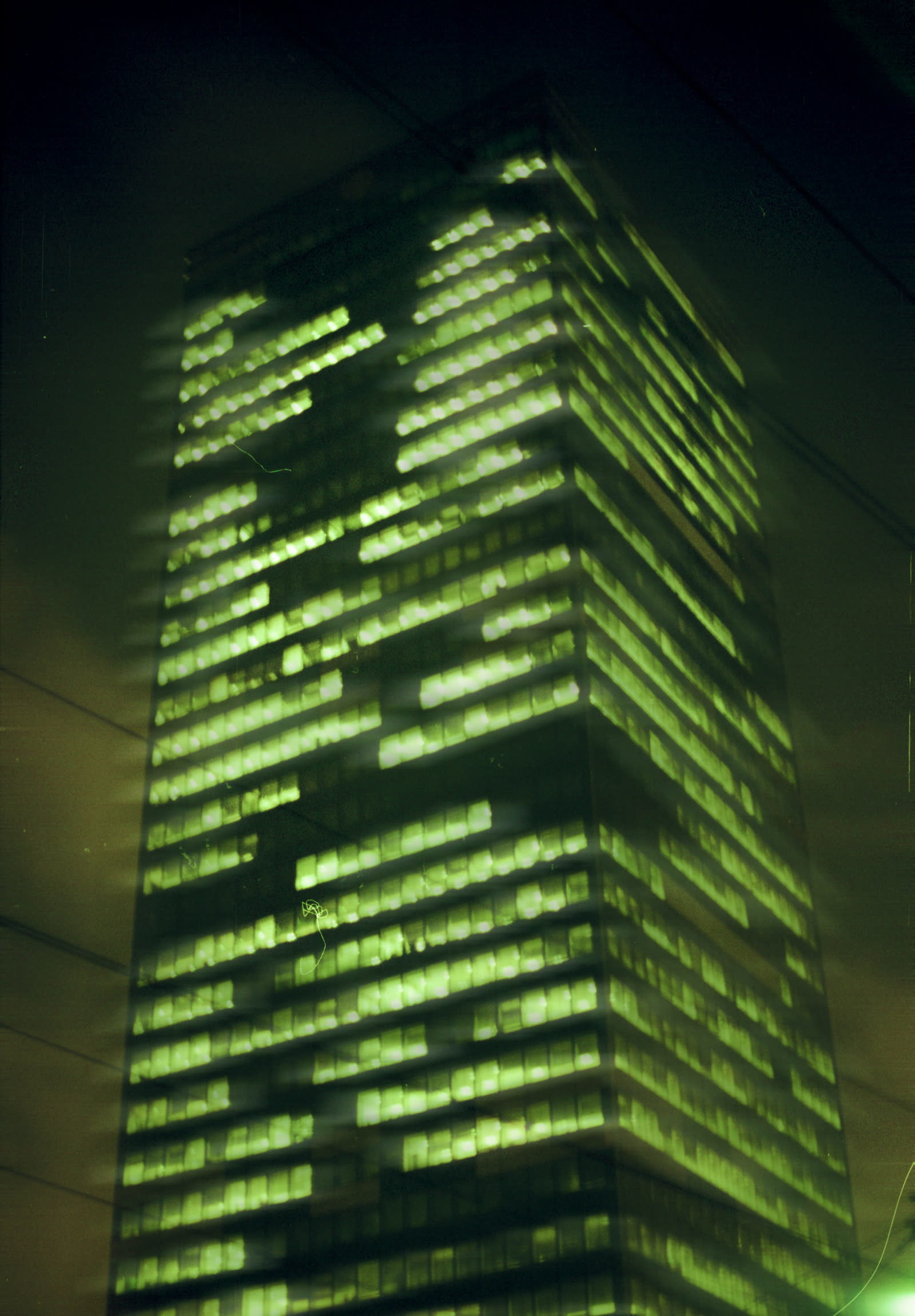 A skyscraper lit green from base to crown, its windows scattered like a code