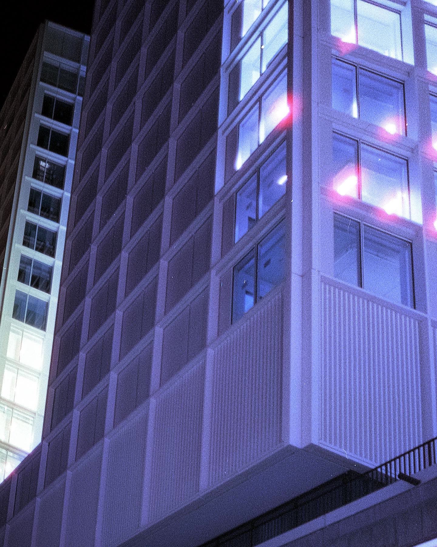 A close-up of an angular building corner at night, blue-lit windows with pink reflections