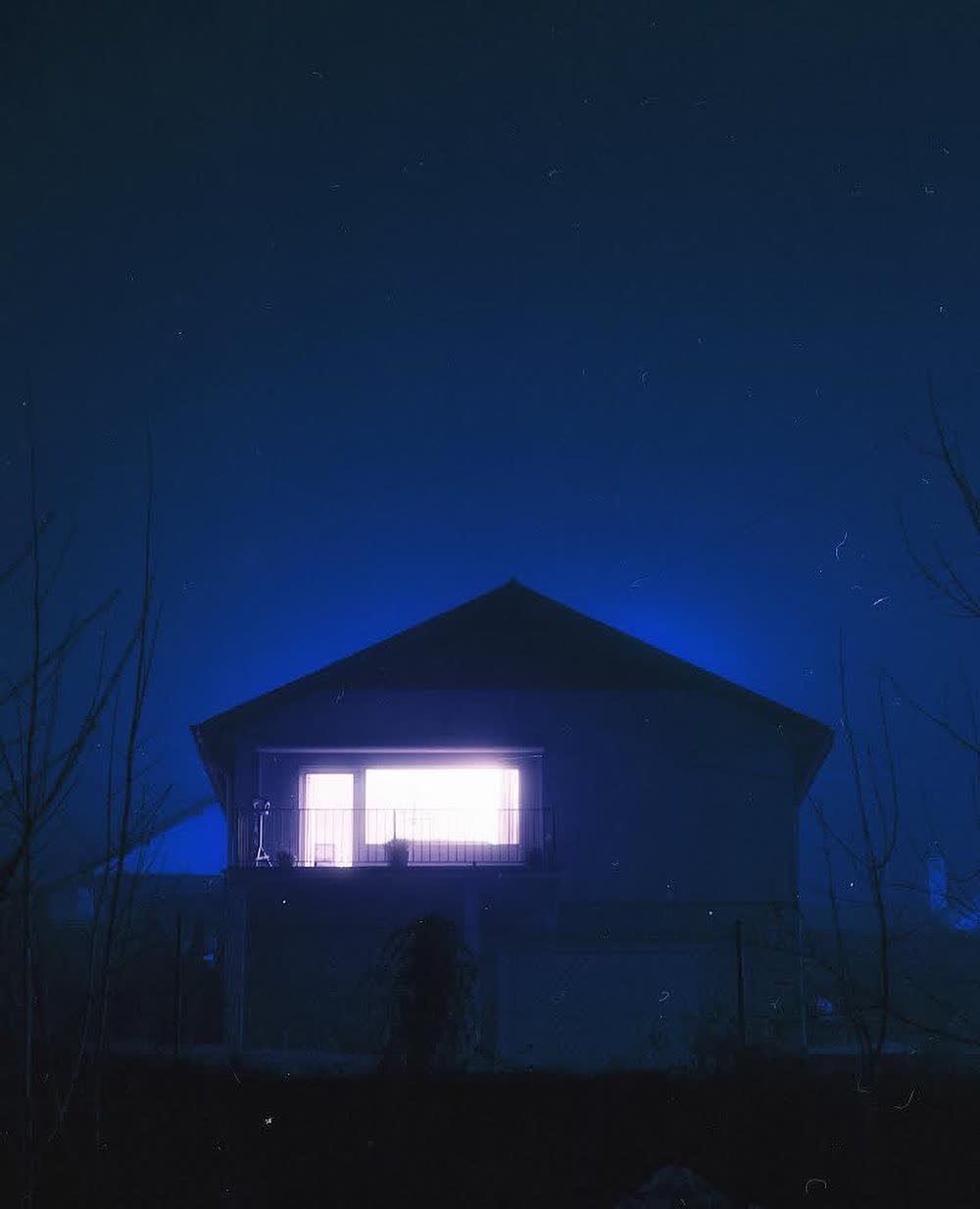 A house glowing deep blue at night, one balcony window lit white