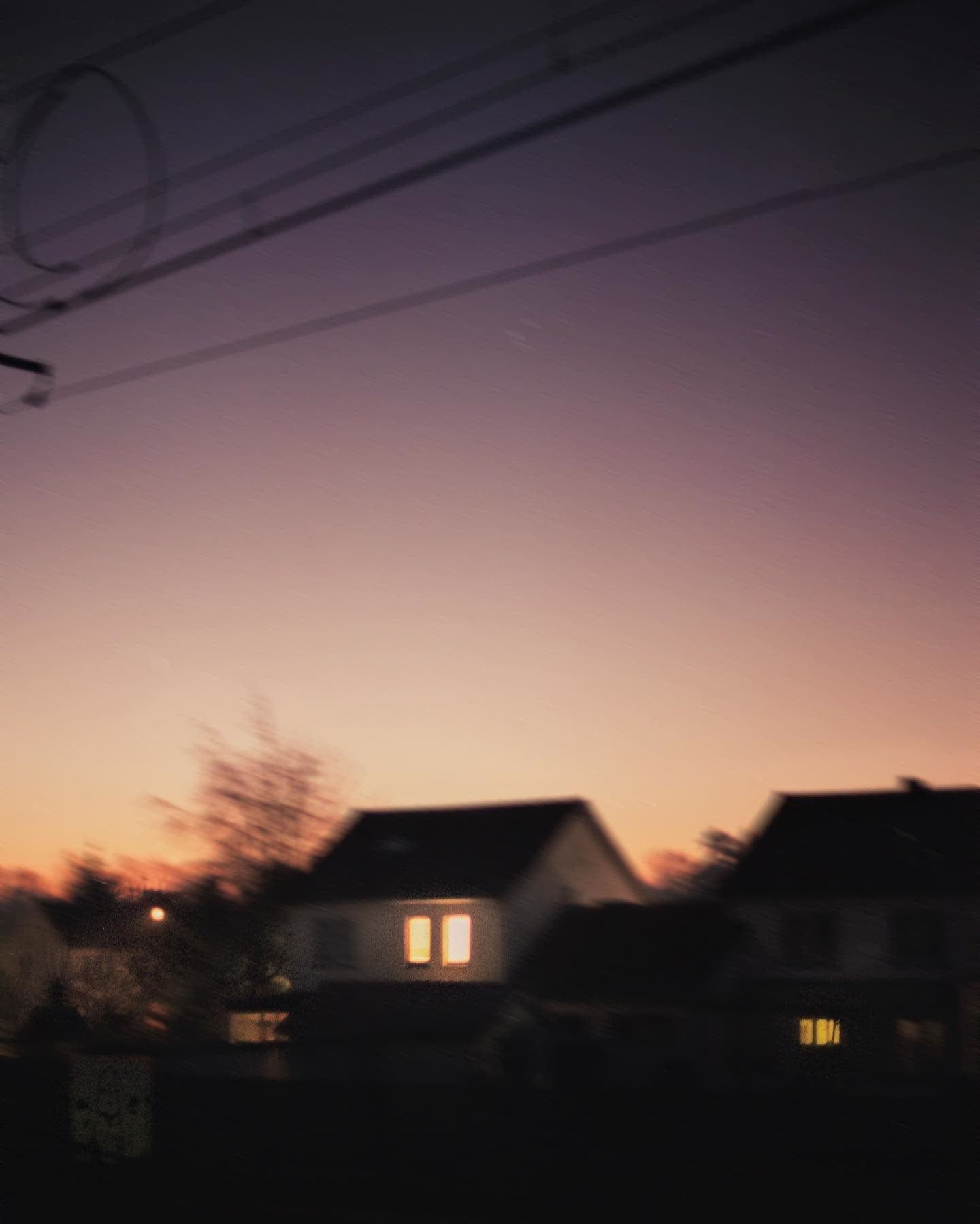Rooftops at sunset, one window glowing warm against the last of the light